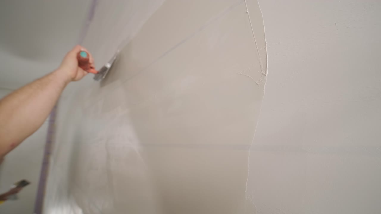 hombre enyesando las paredes con la masilla de acabado en la habitación con la espátula de masilla