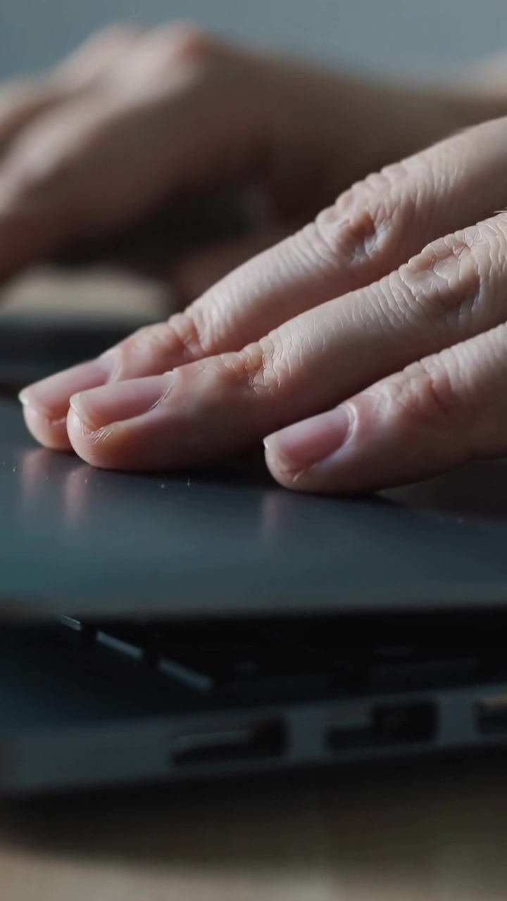 Video verticale: Un dispositivo scorre sulla tastiera di un laptop, mani adulte si muovono e digitano per inserire testo