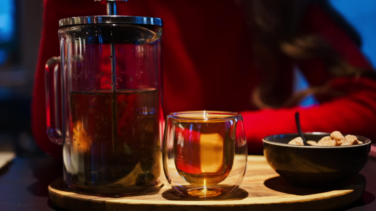 Close up of a woman pressing down the tea leaves with the help of a French press near a cup of tea at a restaurant