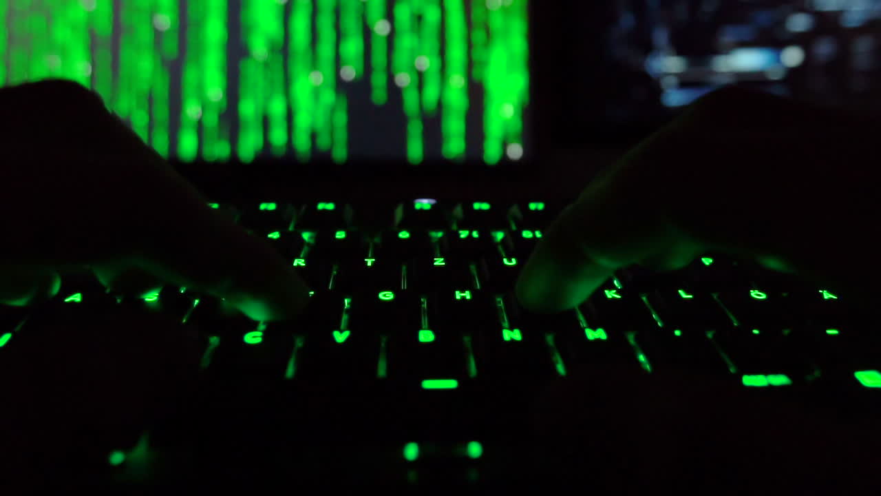 Hands typing on a backlit keyboard with green code on screen