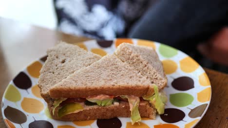 little kid with dirty hands picking up a quarter piece of cut up sandwich with whole wheat bread, pickles, and lettuce