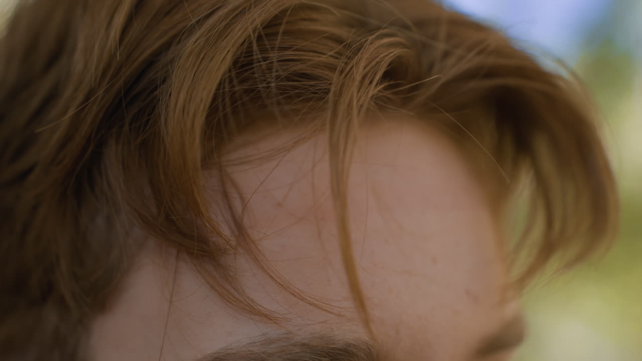 Close up view of white man brown hair loosening white headband in lonely forest, blurred trees backdrop, wisps of hair framing forehead, hands pulling fabric strap under sunlight, introspective mood