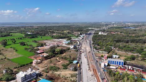 drone view of chennai's evolving landscape. a new highway is built through agricultural fields, leading towards distant industrial areas and lakes. ideal for infrastructure and development