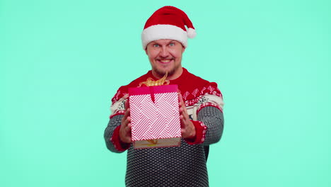 Cheerful-man-in-Santa-sweater-presenting-one-Christmas-gift-boxes,-stretches-out-his-hands-to-camera