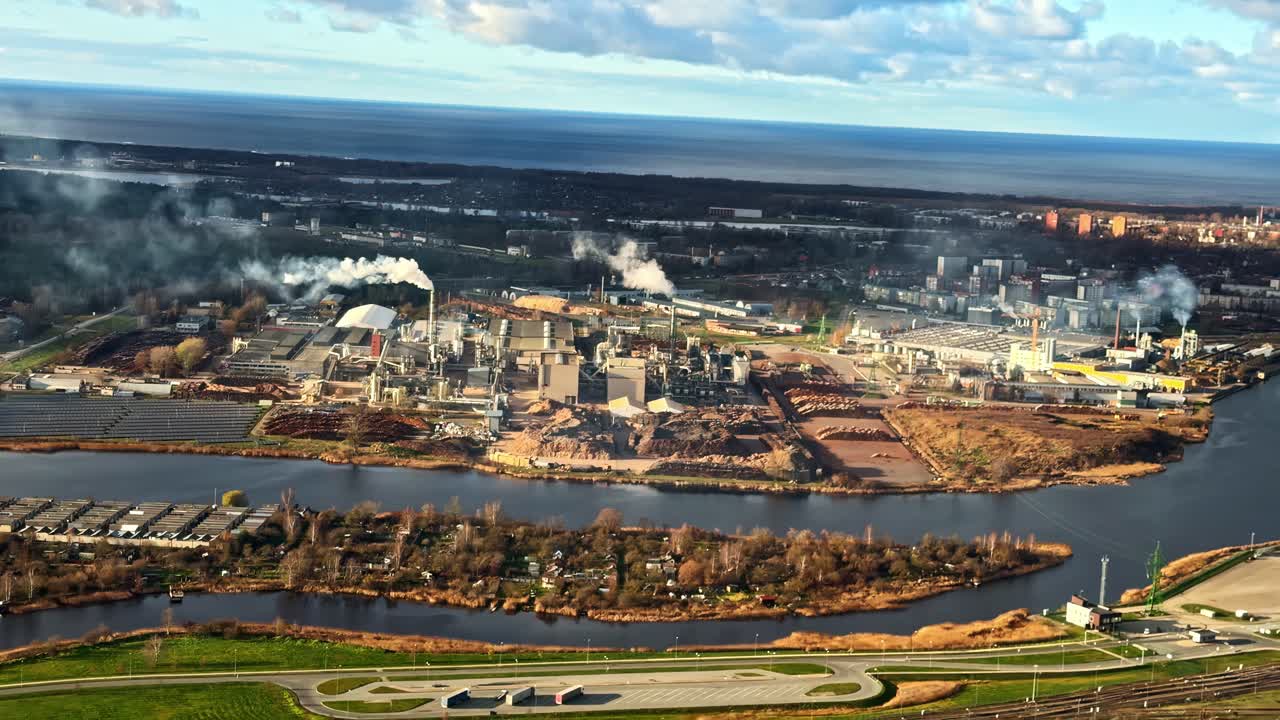 Højtliggende luftfoto af stort industrikompleks med røg og flodlandskab nedenfor