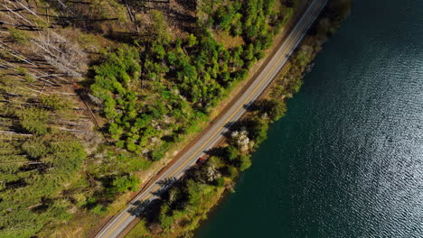 highway along the river at the foot of the mountain. red car goes by the road meeting white car. bird's eye perspective.