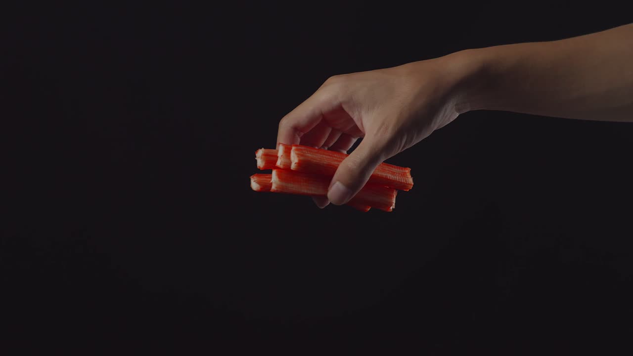 рука, держащая крабовые палочки на черном фоне