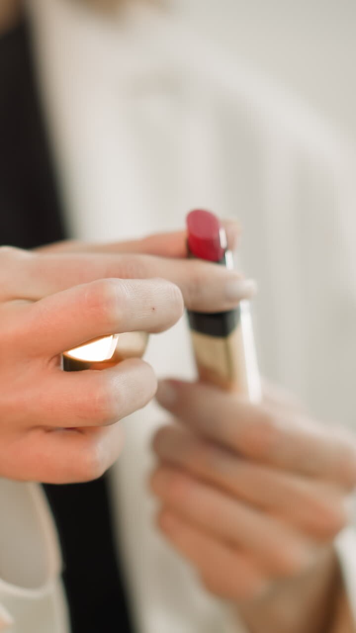 Hands of woman turning tube of lipstick to paint lips red on blurred background. Elegant female does makeup using high quality products closeup