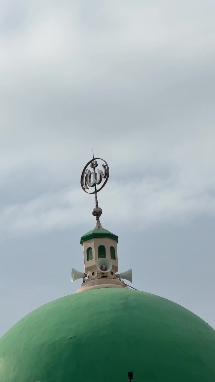 Grüne Moscheekuppel mit islamischer Kalligrafie vor bewölktem Himmel