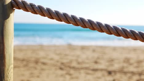 vista aislada de una cuerda con la playa y el océano al fondo - la cuerda actúa como barandilla de seguridad para un paseo marítimo