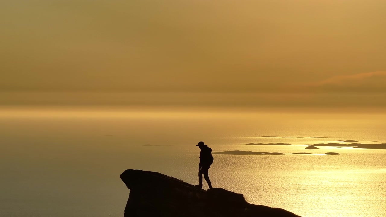 Silhouette di escursionista che cammina su una montagna costiera norvegese sotto il sole di mezzanotte; zoom del drone