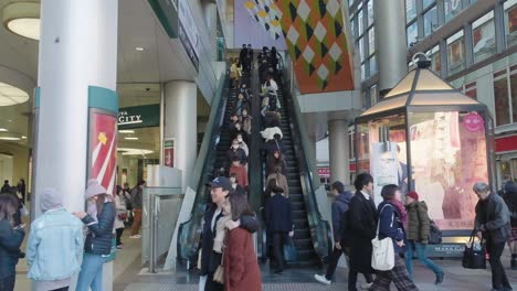 people going up and down an escalator in a shopping mall in shibuya, tokyo, japan. slow motion