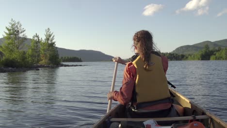 female paddles a canoe on a lake with mountains in the background during sunset in slow motion