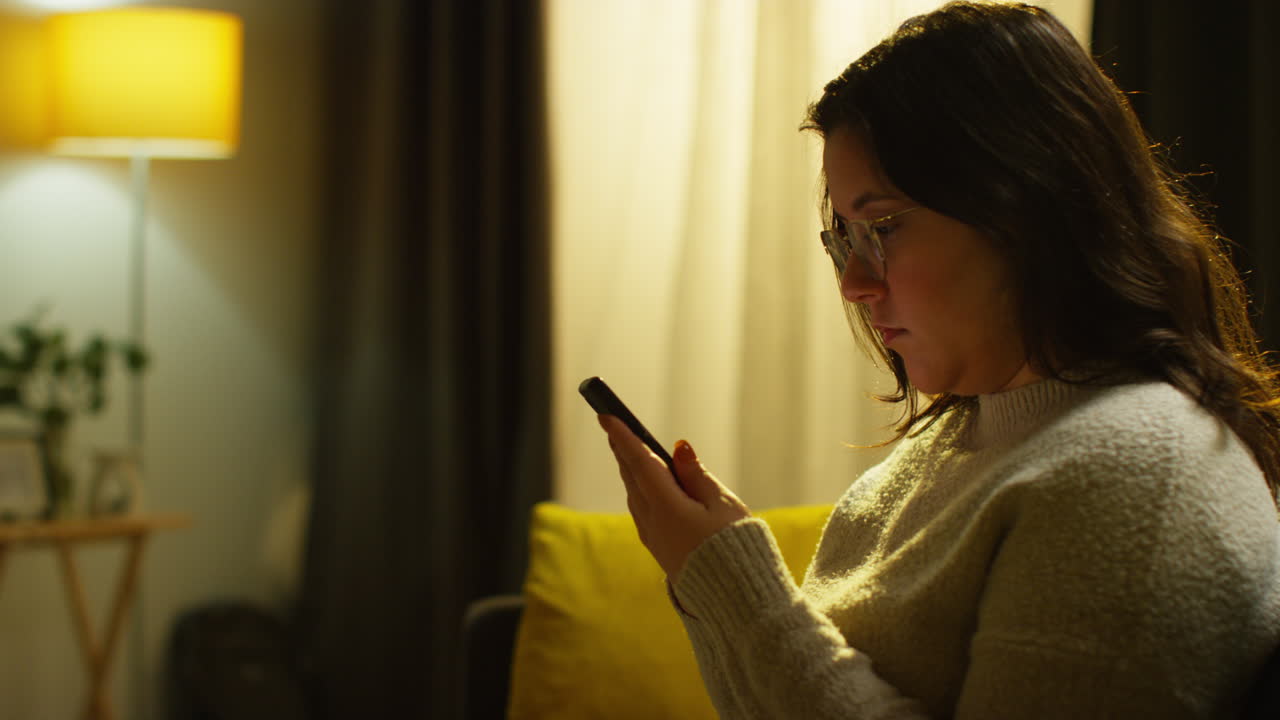 mujer joven pasando la noche en casa sentada en el sofá con el teléfono móvil desplazándose por internet o redes sociales 1