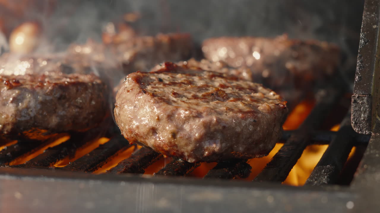 Primo piano di hamburger di manzo al barbecue sfrigolanti cotti alla griglia, al rallentatore