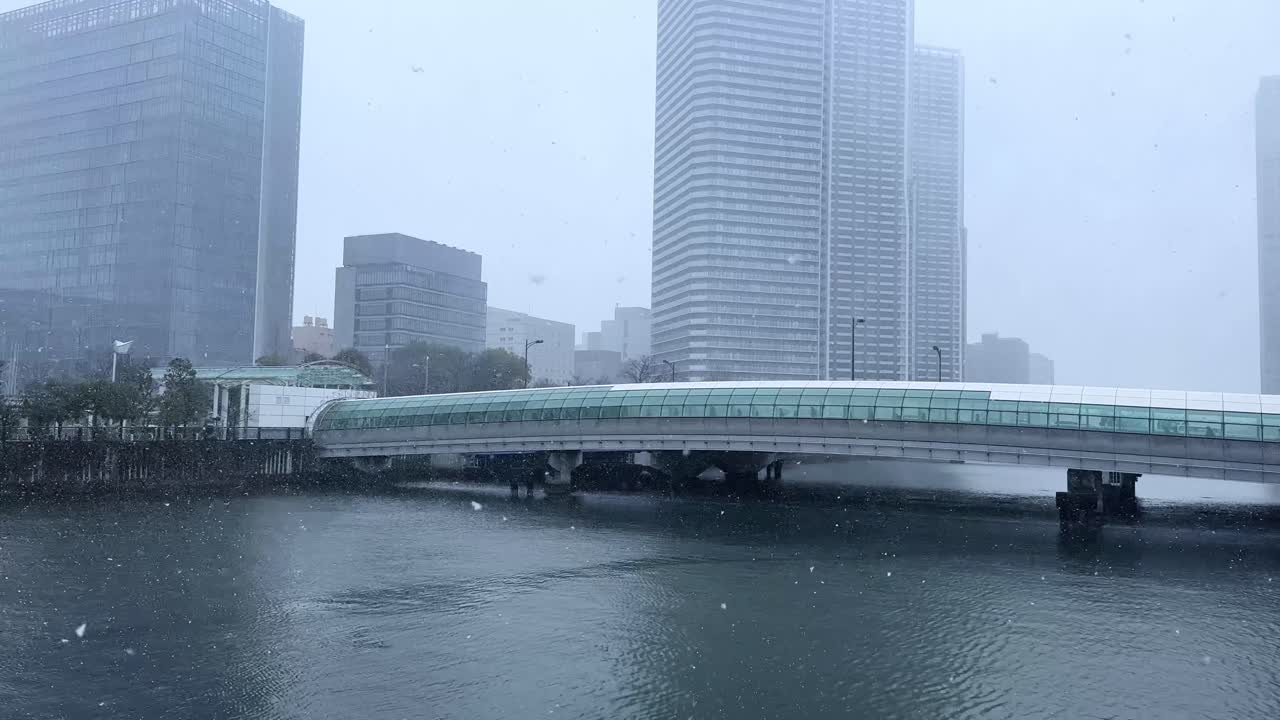 Snowfall in Tokyo cityscape, showing a modern bridge and skyscrapers over water