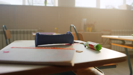 School-supplies-lying-on-desk-in-classroom.-Notebook-and-pencil-case-on-table