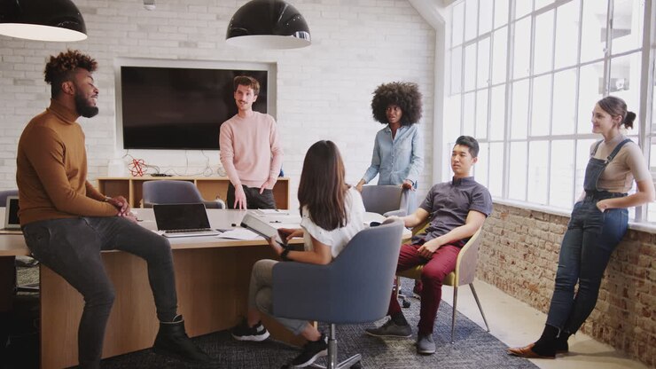 Six millennial creative coworkers in discussion in an office meeting room, full length