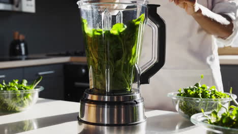 woman making a green smoothie in kitchen