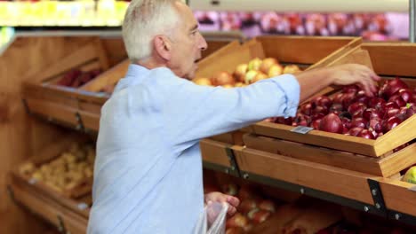 hombre mayor recogiendo manzanas en el supermercado