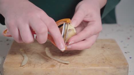 mujer pelando la piel de una patata pequeña sobre una tabla de cortar de madera, cerrada