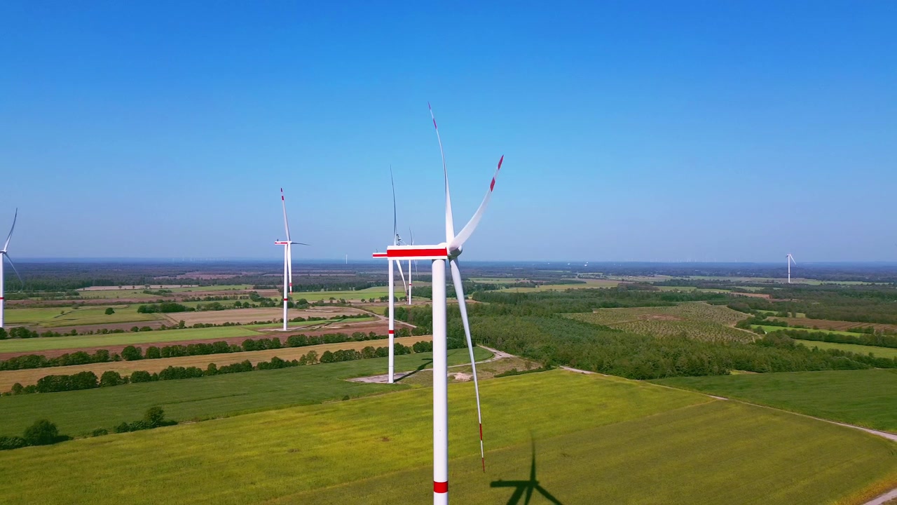 Riprese aeree con drone che mostrano molteplici turbine eoliche attraverso campi aperti, evidenziando infrastrutture rinnovabili all'interno di un ampio paesaggio rurale