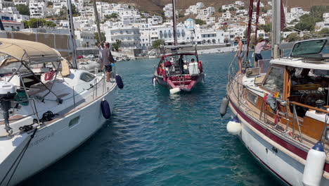 greece, astypalea harbor, a red sailboat docking with astern and trying to land between two boats on heavy wind. people trying to protect their boats with fenders in their hands and helping the boat.