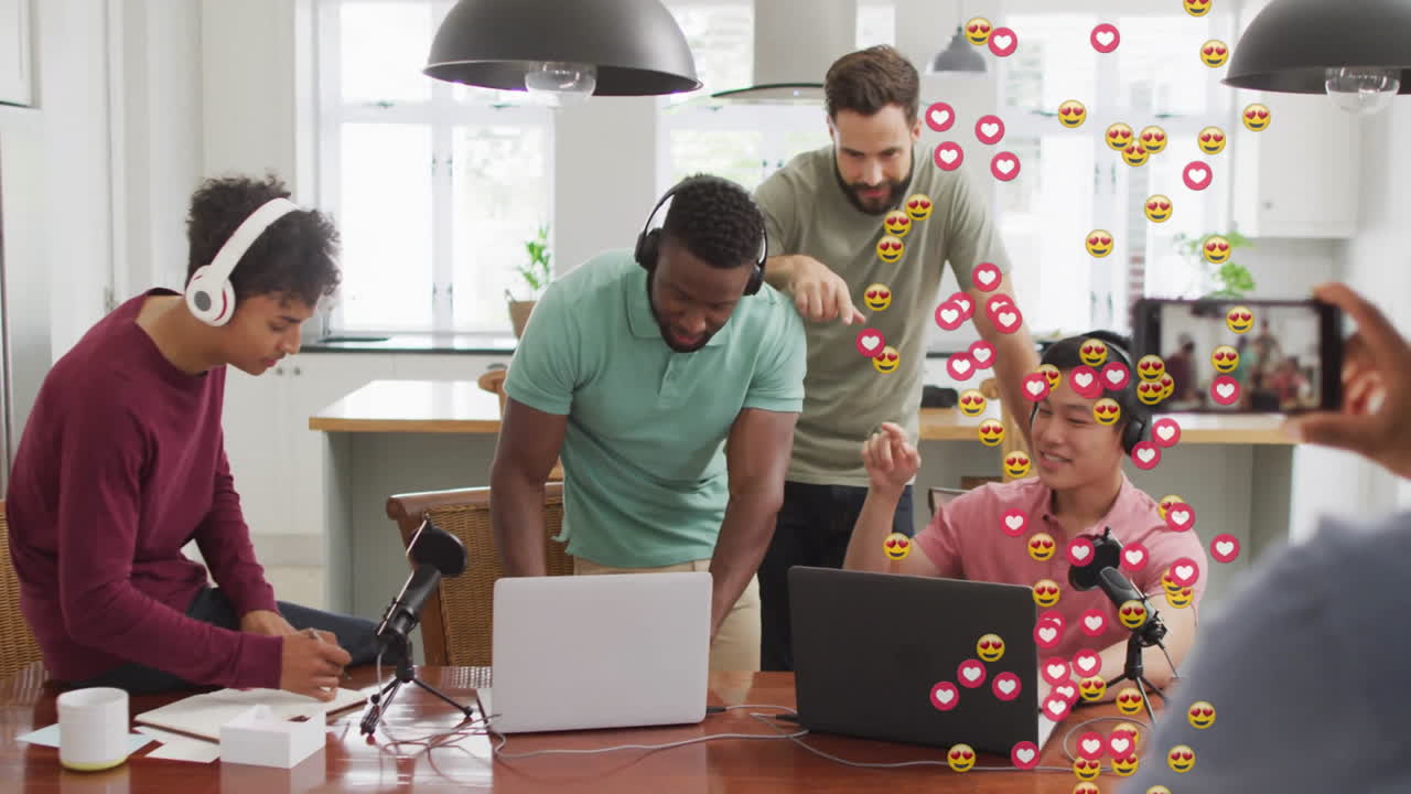 Four men working in studio, livestreaming content creation with floating heart emojis on smartphone