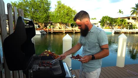 Macho-Caucásico-Plateando-Champiñones-A-La-Parrilla,-Brochetas-De-Shish-Kabob,-Canal-De-Agua-En-El-Fondo