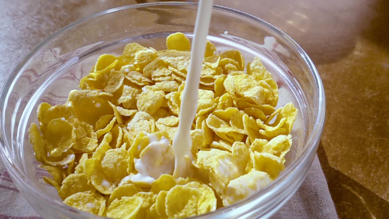 朝のボウルに脆い黄色いコーンフレイク 牛乳の美味しい朝食 ローテーション・トラッキング・ショットのスローモーション