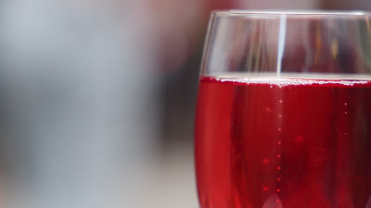 Red cocktail glass in sharp focus, blurred people and soft evening lighting, shallow depth outdoors