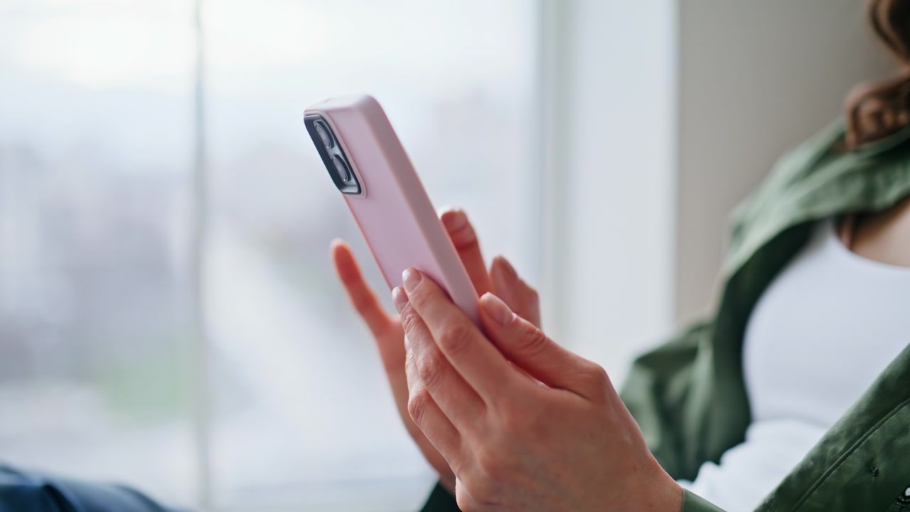 女性が携帯電話をスクロールする手元のクローズアップ。若い女性がSNSを閲覧