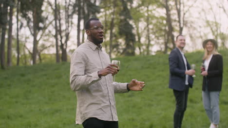 middle aged man dancing while holding a wine glass in the park