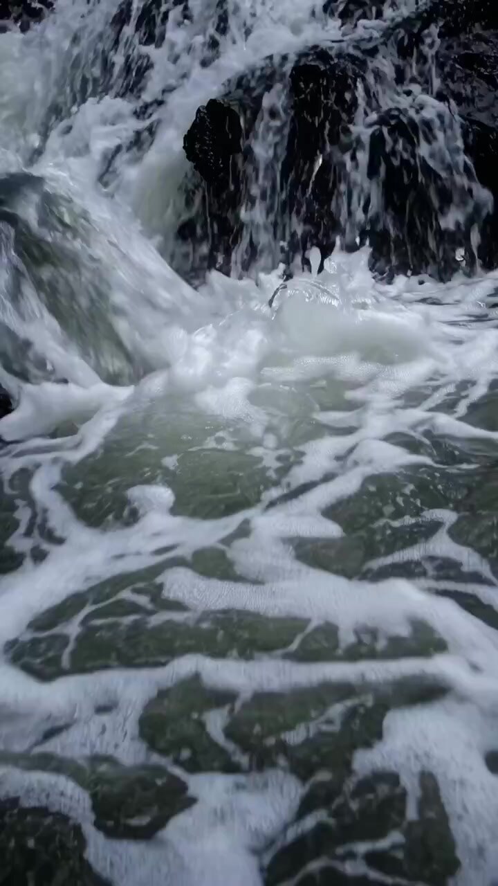 Primo piano di acqua impetuosa e schiuma bianca su rocce scure