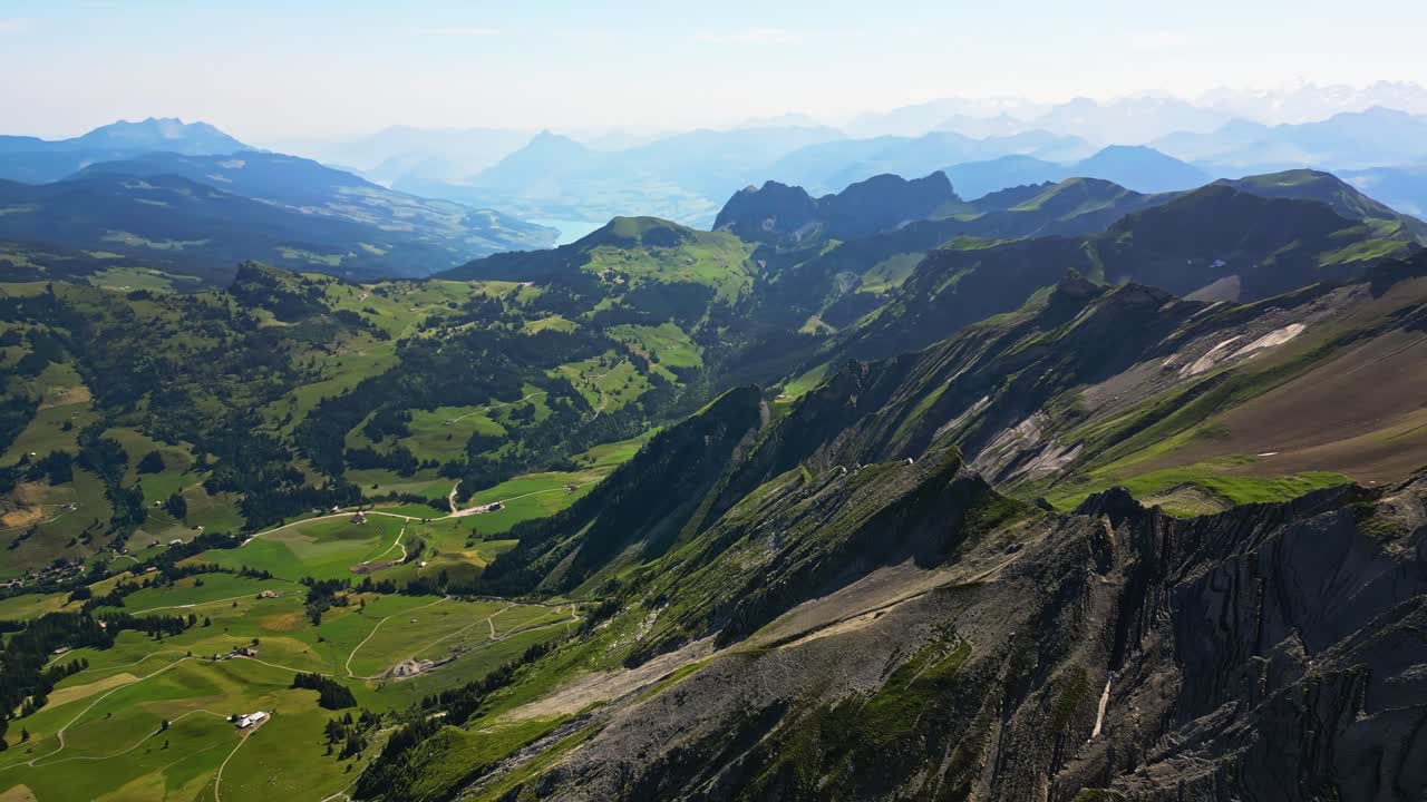 vista desde un pico alto, con vistas a un pueblo con una gran cordillera en el fondo, rodeado de paisaje verde