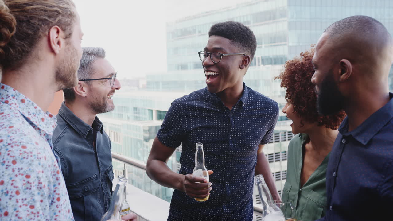 Five creative business colleagues talking and laughing over drinks after work in the city, close up