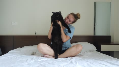 young woman sitting on bed holding and cuddling her black cat, slow mo