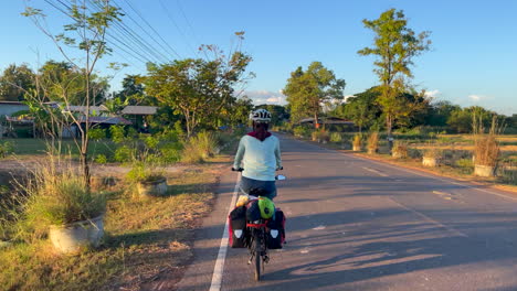 a dynamic footage of an empty road in a golden hour while woman riding her bike with panniers passes by and overtakes