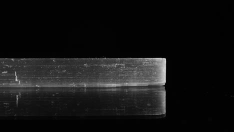 side view of clear, transparent selenite shard as it pans across a black background, studio-lit for maximum clarity