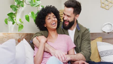video portrait of happy diverse couple sitting in living room embracing and smiling