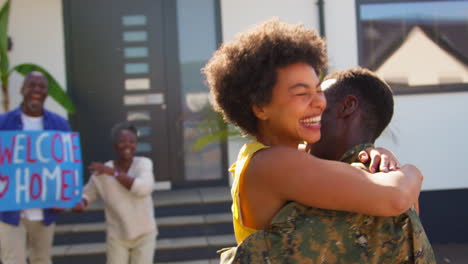 multi-generation family with parents and wife welcoming army soldier home on leave with banner