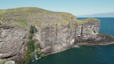 cliffside waterfall cascading into the ocean with rugged terrain in coastal scotland