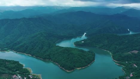 Drone-backwards-shot-of-Feicui-Dam-surrounded-by-green-scenery-of-Taiwan-during-mystic-cloudy-day