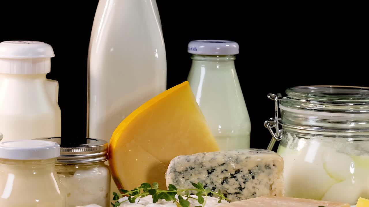 A variety of cheeses and milk bottles arranged on a black background, showcasing dairy richness.