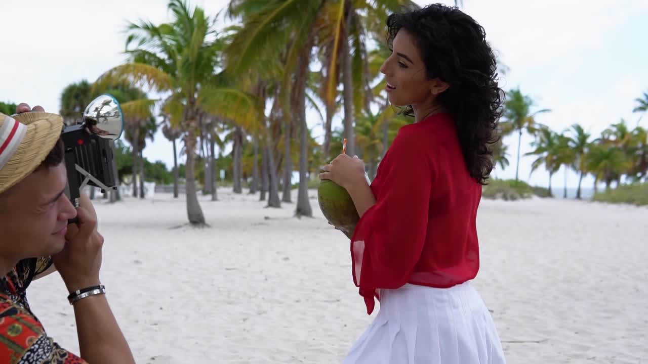 Video of tropical beach picnic in Hawaii featuring a woman holding a coconut, surrounded by palm trees and white sand. A vibrant moment of island leisure, natural beauty, and relaxed coastal charm