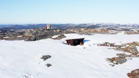 dos turistas excursionistas en la cima de una montaña cubierta de nieve con una pequeña cabaña de invierno de madera
