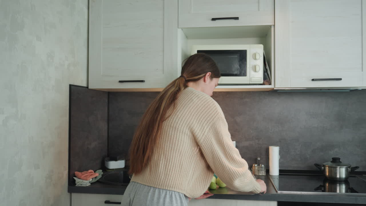 Donna in attesa osserva serenamente il fornello in un ambiente cucina accogliente, indossando un comodo maglione.