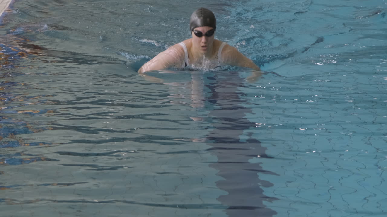 실내 수영장에서 모자와 고글 수영 평영을 가진 젊은 여성 수영 선수의 정면 샷