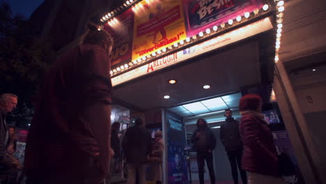 panning low rotation around people walking in front of theatre entertainment buildings illuminated in twilight, madrid.