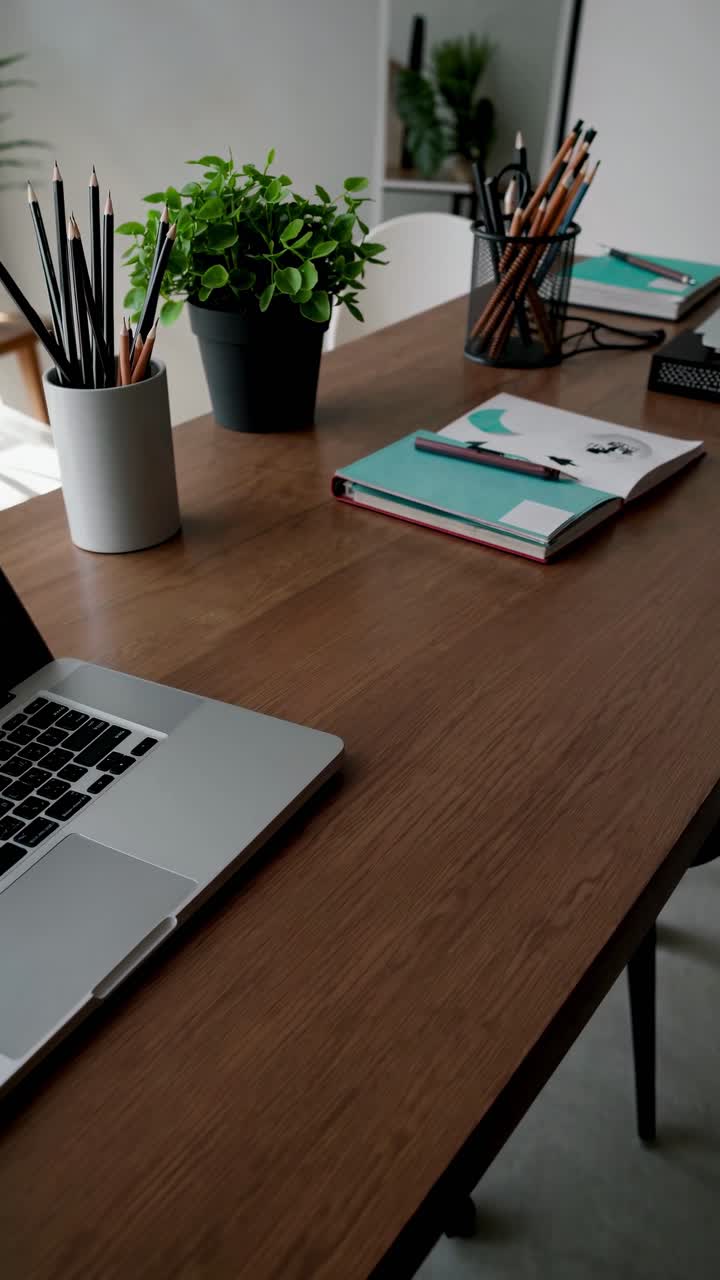 A modern workspace with a laptop, notebooks, and plants on a wooden desk